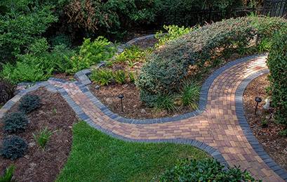 A landscaped garden with brick walkways, grass areas, mulch areas, and various types of bushes.